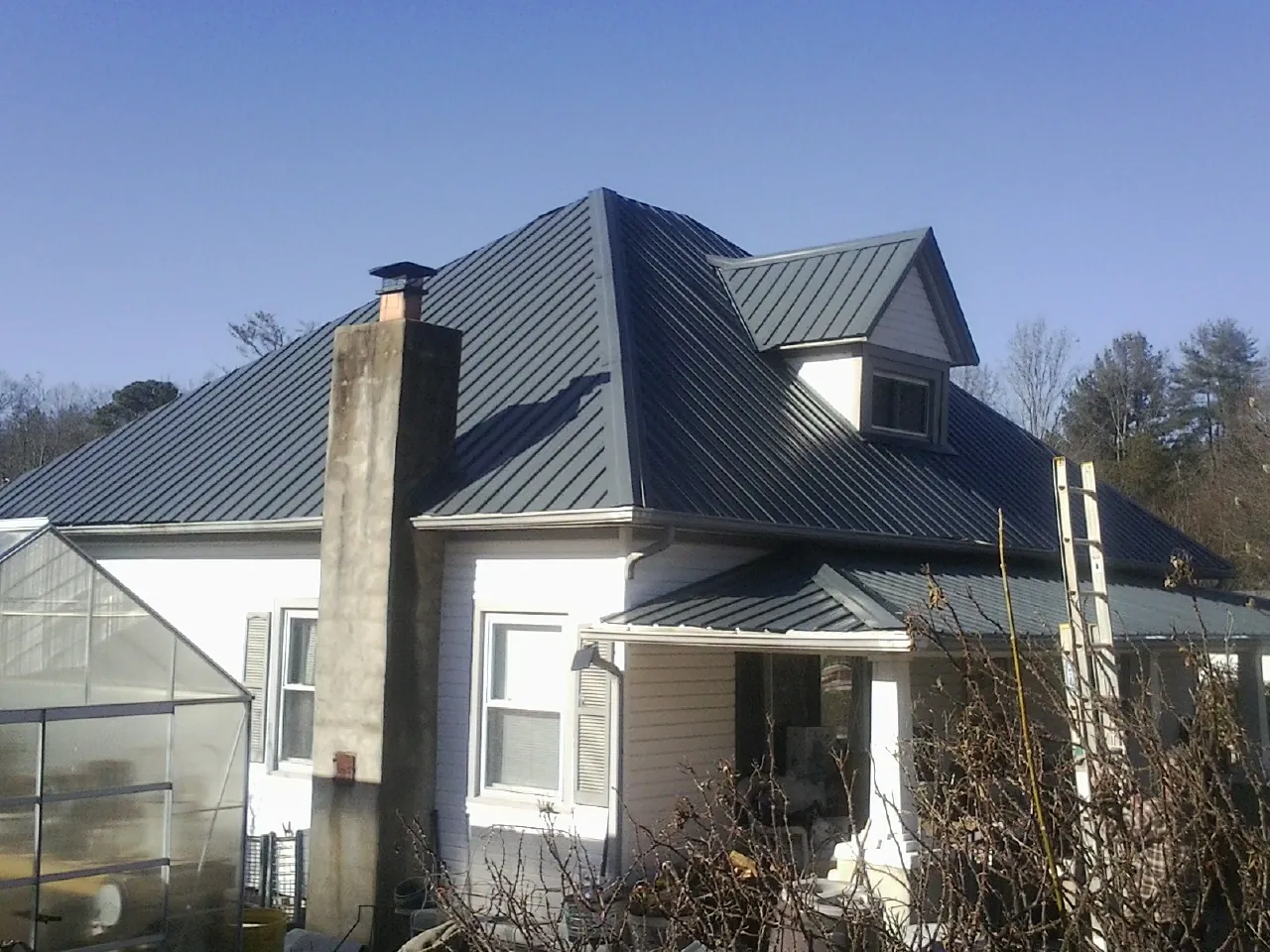 Dark blue standing seam metal roof on a white farmhouse with dormer — Slate & Tile Roof Repair by Roofing Brothers in Holladay
