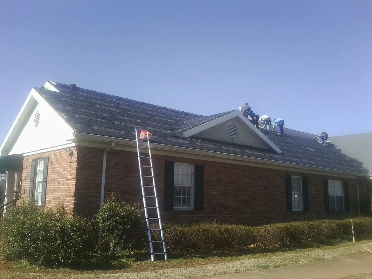 Crew tearing shingles off a brick ranch roof with a ladder set — Emergency Roof Repair work by our crew in Holladay