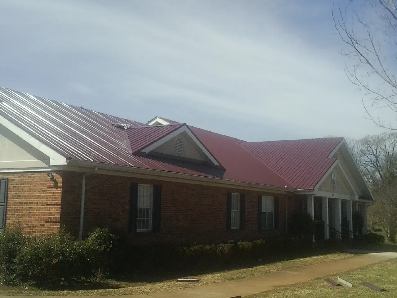 Red metal roof with gabled entries on a long brick building, from a Hail Damage Roof Repair job in Holladay