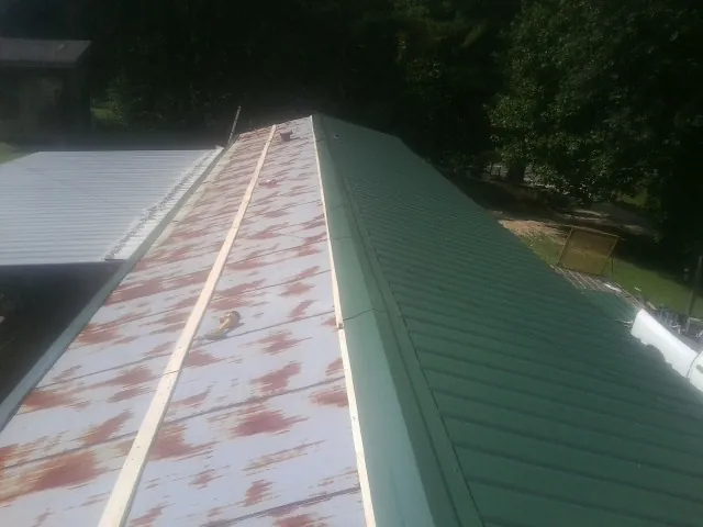 Old rusted panels beside newly installed green metal roofing — Wind Damage Roof Repair by Roofing Brothers in Holladay