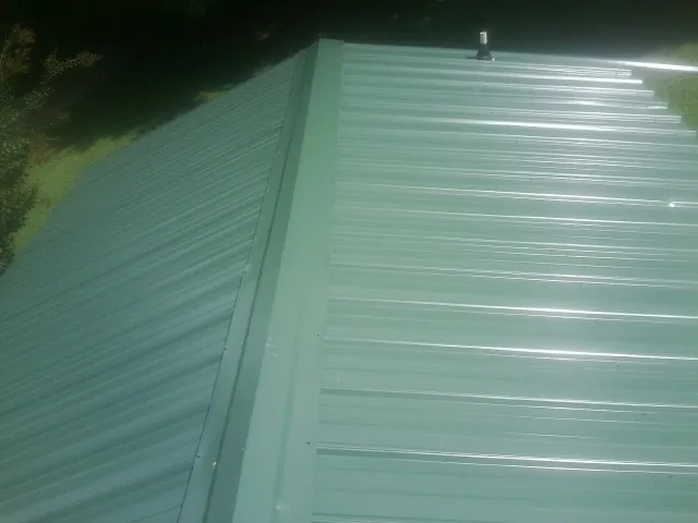 New green metal panels meeting at the ridge of a roof — Flat Roof Repair work by our crew in Holladay