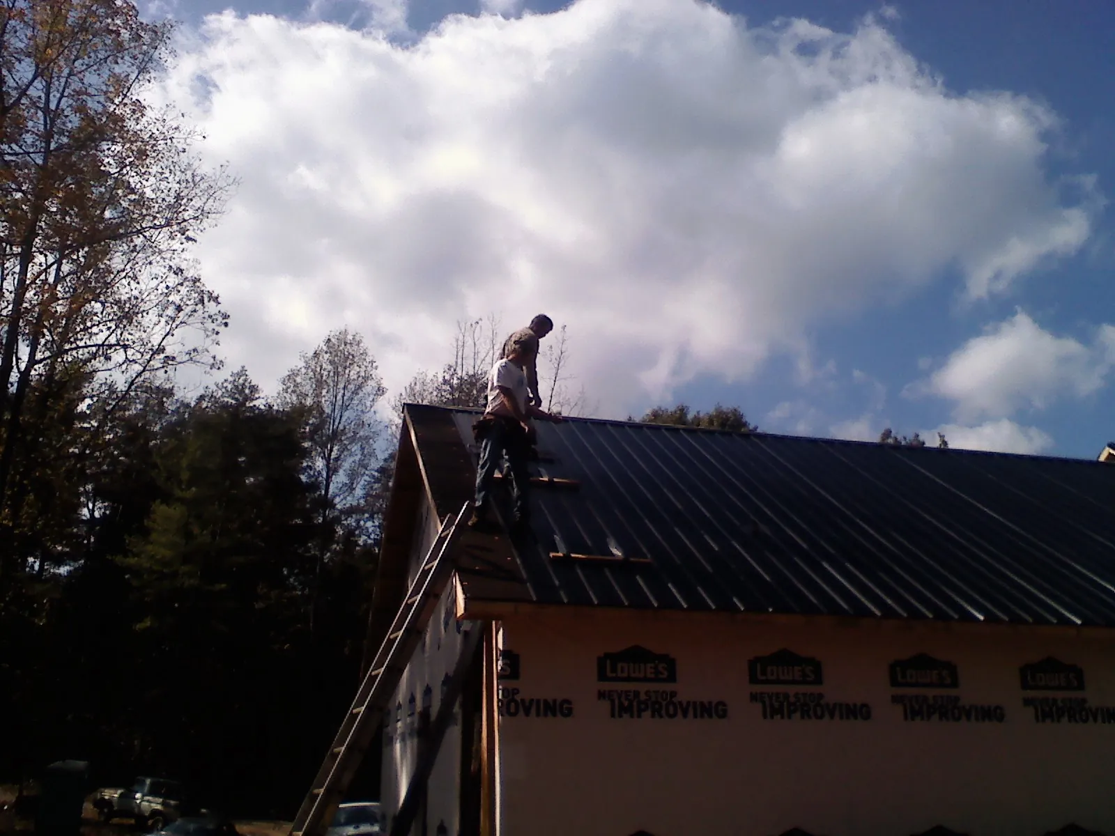 Roofer fastening dark metal panels high against a cloudy sky, from a Roof Inspection job in Holladay