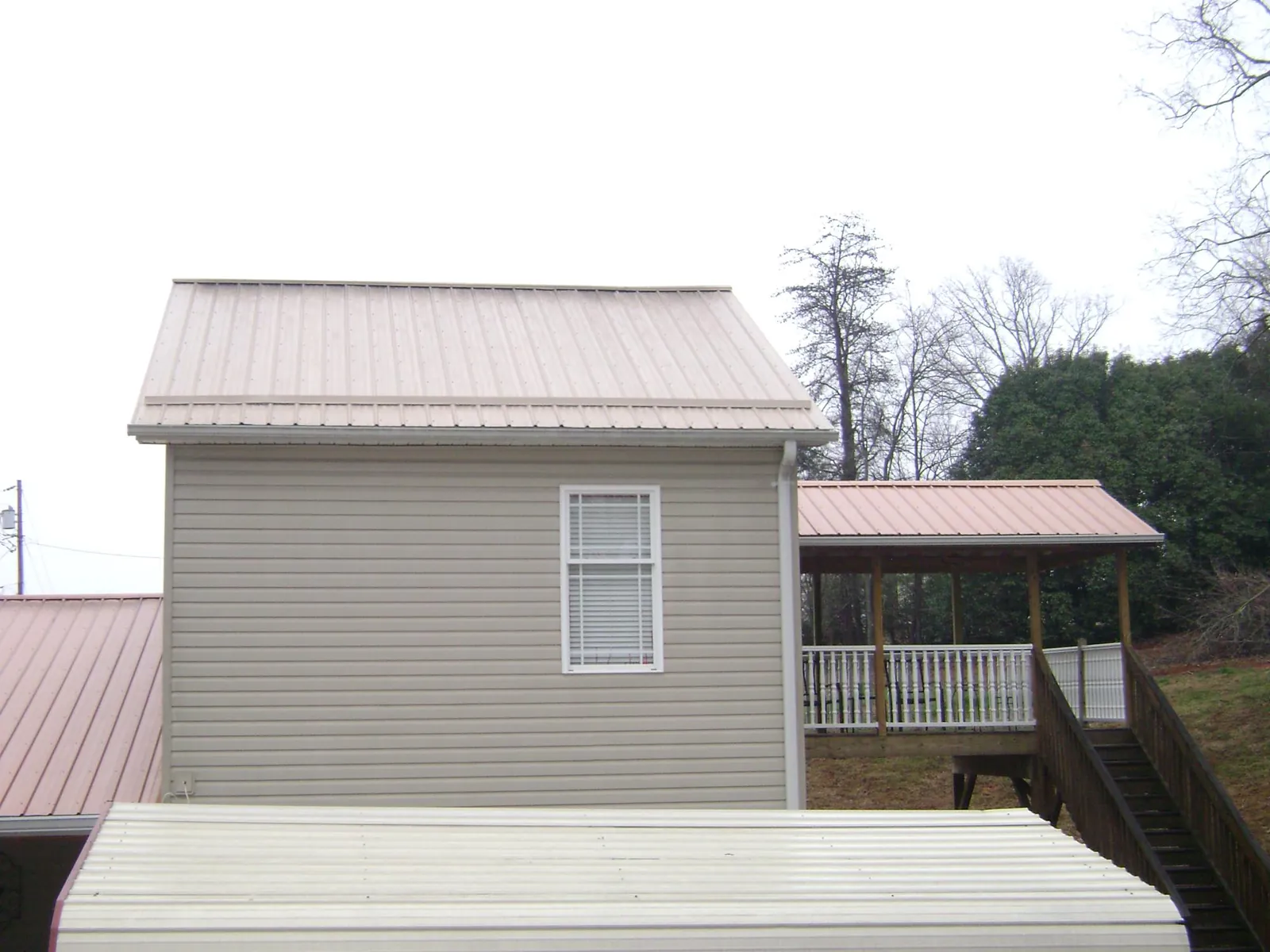 Tan metal roofs on a two story addition and attached porch, from a Roof Replacement job in Holladay